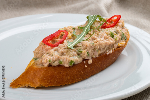 Bruschetta with fish tartare on a white plate, on a textile background