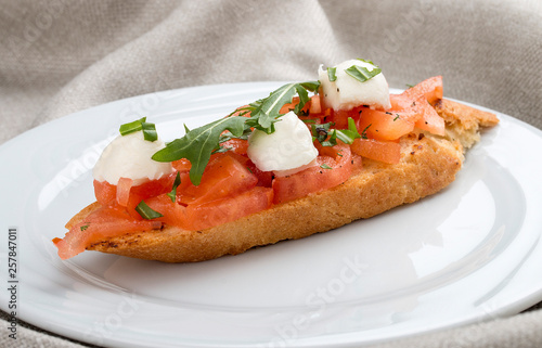 Bruschetta with tomatoes and mozzarella on a white plate, on a textile background