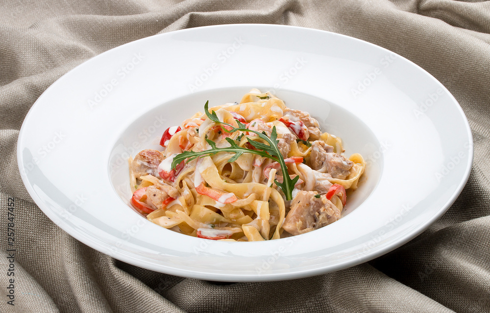 Tagliatelle with rabbit and pepper, with cream sauce in a white plate. On textile background