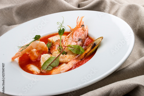 French bouillabaisse fish soup with shrimp, mussels and scallop. In a white plate on a textile background