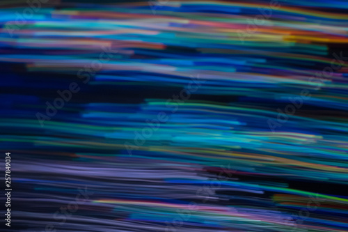 Blurry horizontal wavy lines. Multicolor neon lights in motion on dark background. Bokeh lens flare glow.