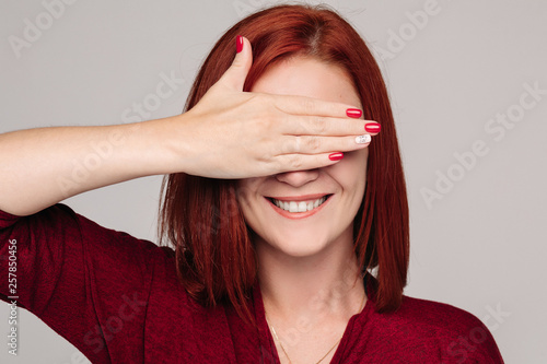 Young pretty lady with red hair in bordo blouse holding eyebrows up and sending kiss. Close up of beautiful woman with red nails holding hadns together near neck. Concept of love to yourself. photo