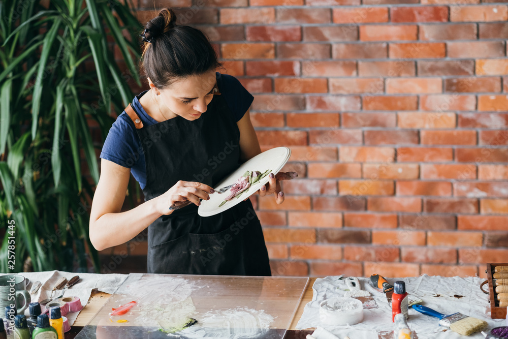 Fototapeta premium Clay art. Ceramic craft. Artist studio workplace. Woman with modeling tools creating flower artwork.