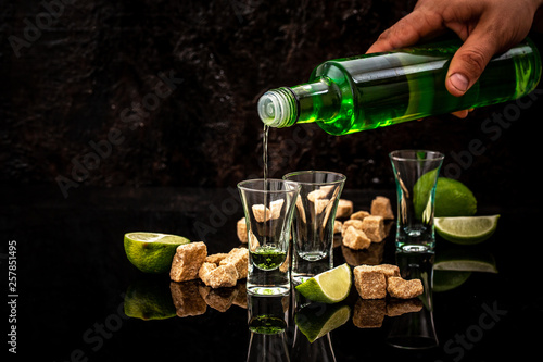 Bottle of absinthe and glasses with burning cube brown sugar on dark background. free space for text. the concept of elite alcohol photo