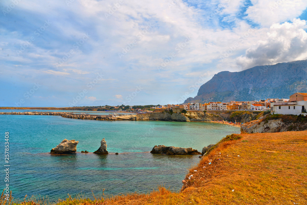 beautiful landscape in small coastal town Terrasini with beach calarossa with Faraglioni di Praiola with turquoise blue water and cloudy blue sky  in background, Sicily Italy Palermo