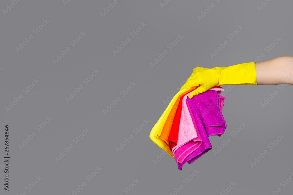 A hand in a rubber glove holds a set of colored microfiber cloths on a neutral background. The concept of bright spring, spring cleaning. A hand in a rubber glove holds a set of colored microfiber cloths on a neutral background. The concept of bright spring, spring cleaning.