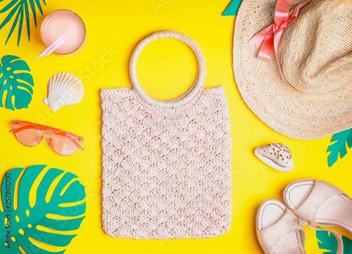 Summer female outfit. Flat lay. Woven hand bag, straw hat, sunglasses, sandals with cocktail , seashells and tropical paper palm leaves on yellow background, top view. Summer holiday vacation.