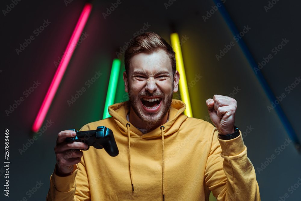 young adult handsome and screaming man looking at camera and holding gamepad - obrazy, fototapety, plakaty 