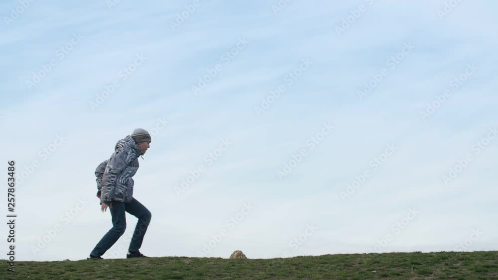 Hilarious boy running and jumping up in a green field with a blue sky in slo-mo Hilarious boy running and jumping up in a green field with a blue sky in slo-mo
