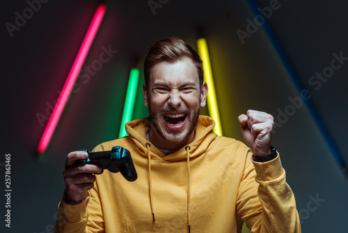 young adult handsome and screaming man looking at camera and holding gamepad photo
