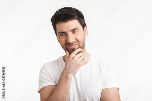 Image of handsome man 30s with bristle in casual t-shirt smiling and touching chin