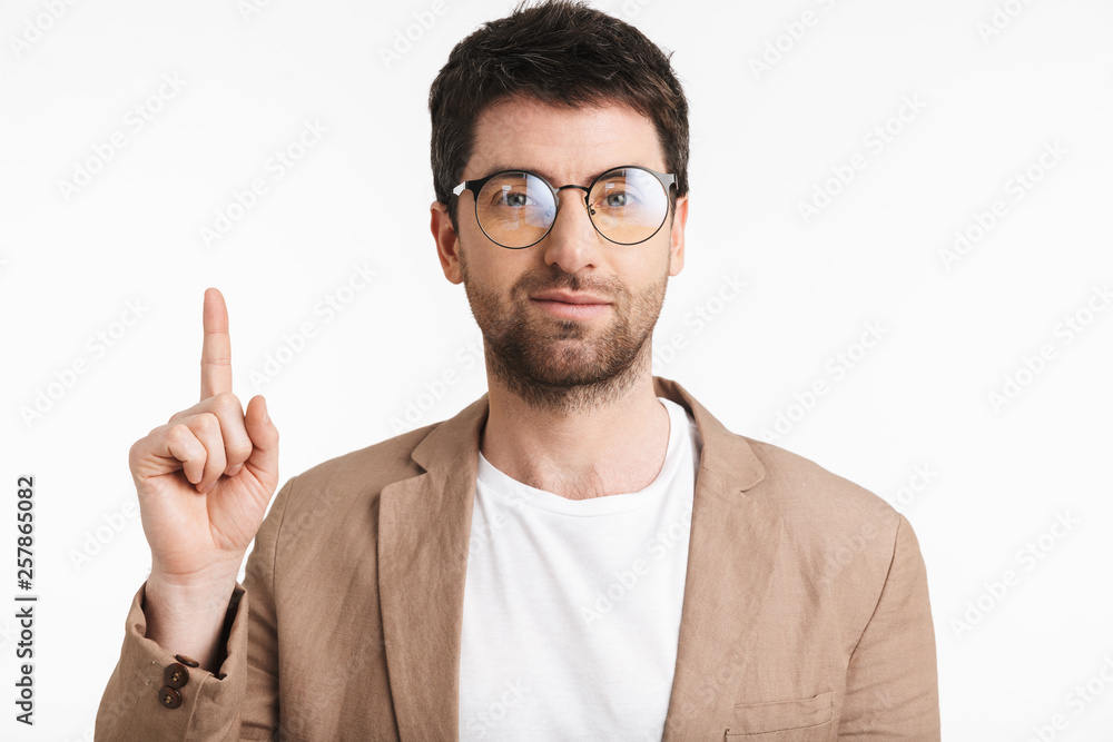 Image of european man 30s with stubble wearing jacket and eyeglasses pointing finger upward at copyspace Image of european man 30s with stubble wearing jacket and eyeglasses pointing finger upward at copyspace