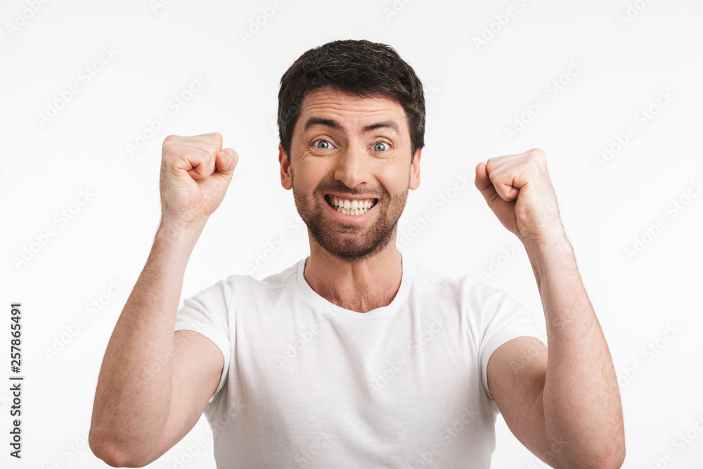 Image of ecstatic man 30s with bristle in casual t-shirt rejoicing and clenching fists Image of ecstatic man 30s with bristle in casual t-shirt rejoicing and clenching fists