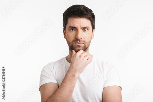 Image of adult man 30s with bristle in casual t-shirt thinking and touching chin
