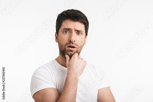 Image of unshaved man 30s with bristle in casual t-shirt thinking and touching chin