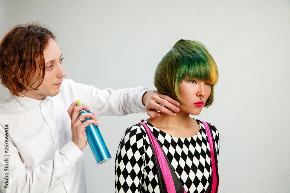 Picture showing adult woman at the hair salon. Studio shot of graceful young girl with stylish short haircut and colorful hair on gray background and hands of hairdresser. Picture showing adult woman at the hair salon. Studio shot of graceful young girl with stylish short haircut and colorful hair on gray background and hands of hairdresser.