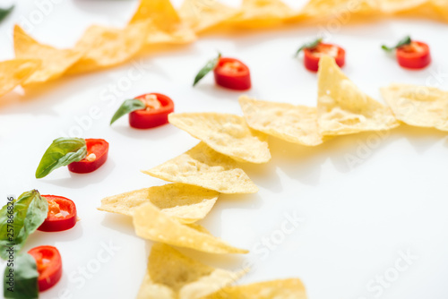 selective focus of chili peppers with basil and tasty nachos on white background
