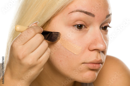 Young blonde applying liquid foundation with brush on white background