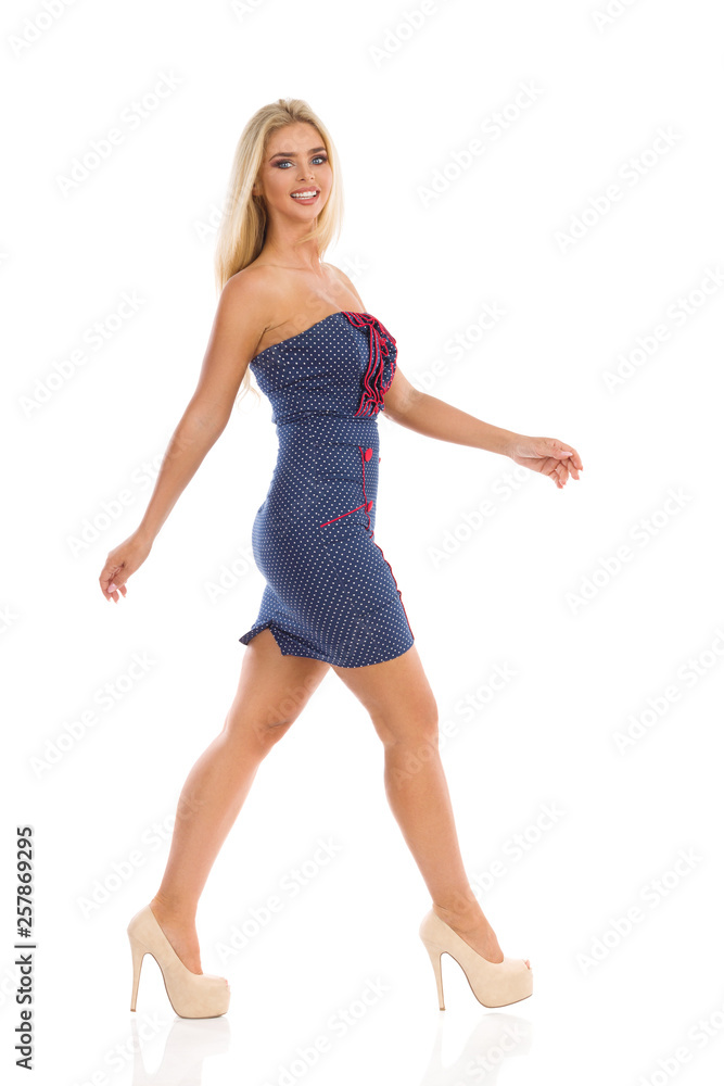 Smiling Woman In Blue Dotted Mini Dress And High Heels Is Walking And Looking At Camera Smiling Woman In Blue Dotted Mini Dress And High Heels Is Walking And Looking At Camera