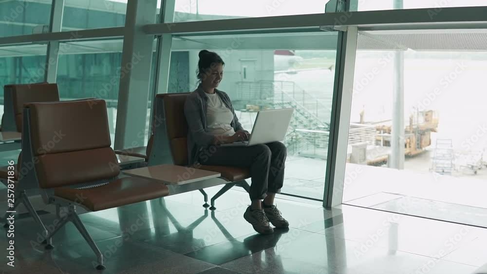Portrait of adult attractive woman sitting at the airport using laptop - surfing internet. People stock footage shot. Portrait of adult attractive woman sitting at the airport using laptop - surfing internet. People stock footage shot.