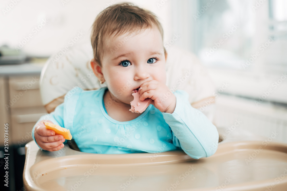 a little girl in a high chair eating a piece of boiled sausage a little girl in a high chair eating a piece of boiled sausage