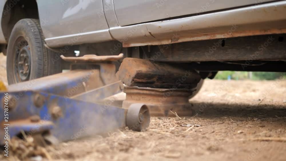 Hands of mechanic using car jack to lift up the truck to repair wishbone control arm and replace the front wheel of the car Hands of mechanic using car jack to lift up the truck to repair wishbone control arm and replace the front wheel of the car