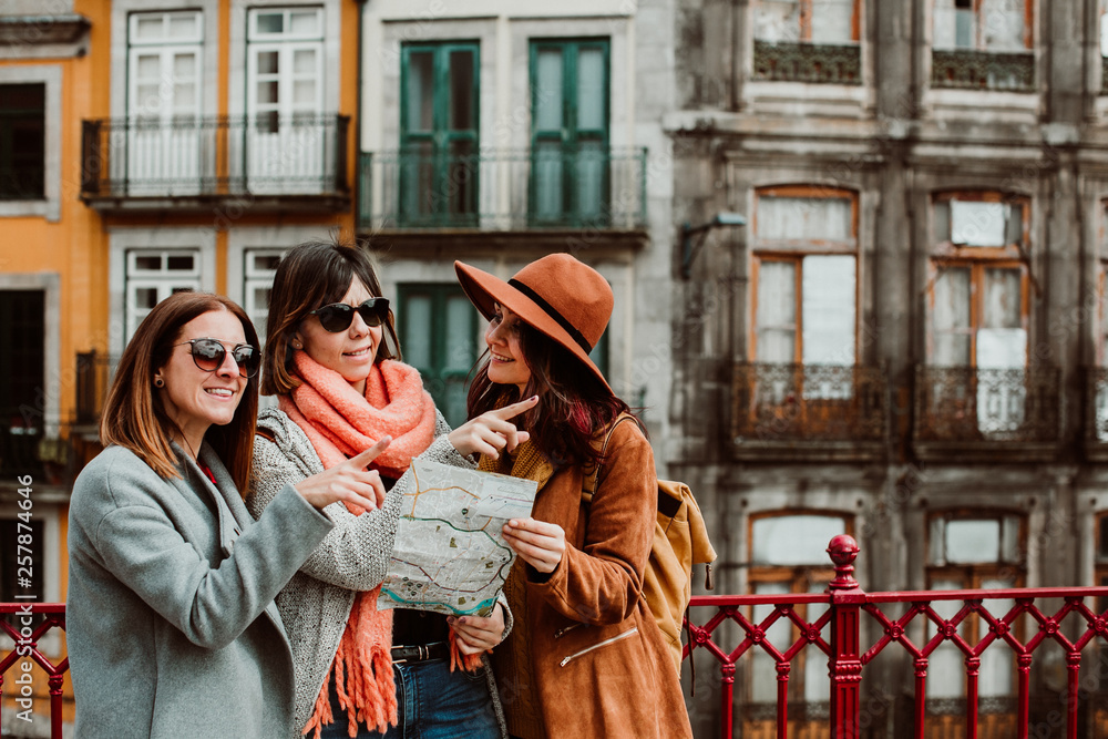 .Three beautiful and funny women traveling together in Porto, Portugal. Standing together carefree and relaxed using their map to locate themselves. Lifestyle. Travel photography