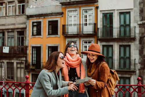 .Three beautiful and funny women traveling together in Porto, Portugal. Standing together carefree and relaxed using their map to locate themselves. Lifestyle. Travel photography photo