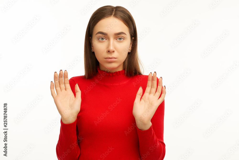 Studio shot of grumpy young woman with irritated expression, makes stop gesture and keeps palms in front, asks to stop panic and be quiet, stands against white background. Body language concept Studio shot of grumpy young woman with irritated expression, makes stop gesture and keeps palms in front, asks to stop panic and be quiet, stands against white background. Body language concept
