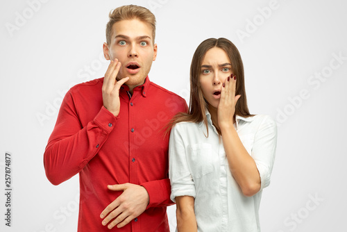 Surprised European people keeps hands on cheeks, shows empathy, amazed by terrible news or revelation, holds hands on face, impressed with something, isolated white background in studio