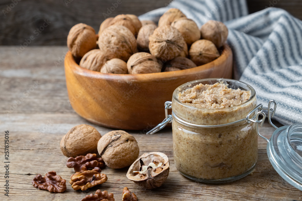 Glass jar of raw organic walnut butter or paste and fresh nuts in bowl on table. Glass jar of raw organic walnut butter or paste and fresh nuts in bowl on table.
