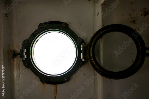 Hinged round window, storm cover on ship looking outside into Mediterranean sea. Porthole view through window on ship to turbulence made by foam of sea water from a high-speed boat on surface of sea.