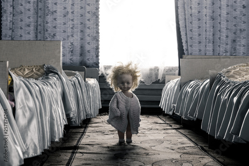 Fotografia, Obraz Creepy doll with yellow hair stands between the beds