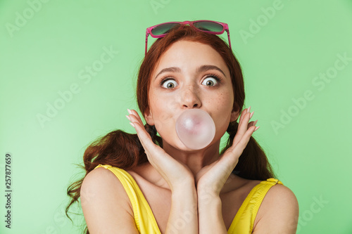 Redhead girl posing isolated over green wall background with chewing gum.