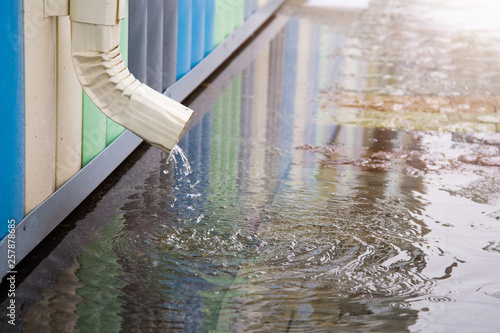 White drainpipe with flooded pavement. Rain water flowing from drain pipe closeup