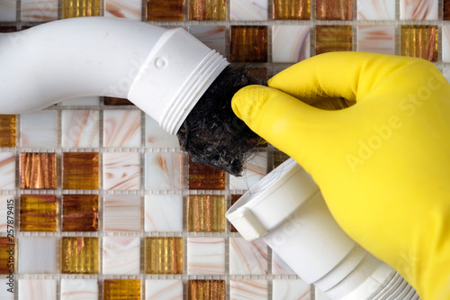 Elimination of blockage in sewer pipes. Hands in yellow gloves disassemble and clean the sink siphon. photo