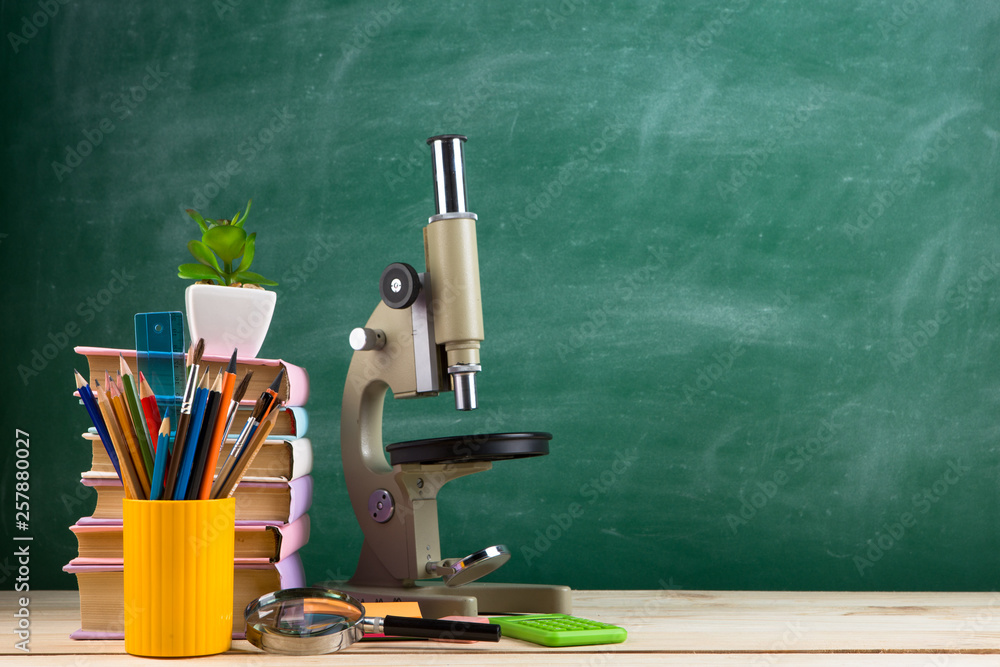 Education and science concept - group of colorful books and microscope on the wooden table in the classroom Education and science concept - group of colorful books and microscope on the wooden table in the classroom