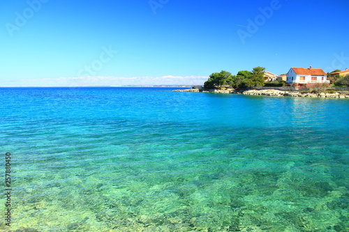 Vacation house on the coast of clear blue sea; Island Ugljan, Croatia. Mountain Velebit on horizon.