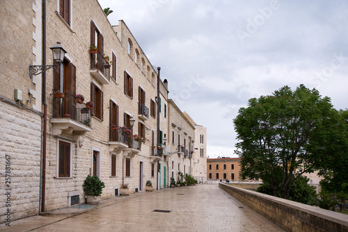 Romantic and historical paved, polished stone sidewalk in Bari, Italy on overcast summer day. White buildings in old town with flower decorations in front of apartments and houses. Concept of travel © lainen