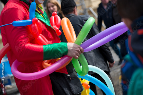 A freelance clown creating balloon animals and different shapes at outdoor festival in city center. School bag, angel wings, butterflies and dogs made of balloons. Concept of entertainment, birthdays