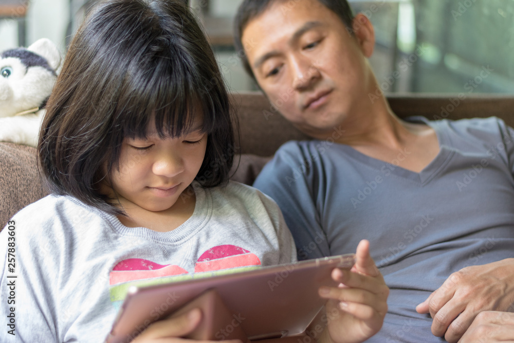 Father and daughter concept. Daddy working on computer notebook hand typing on keyboard while Asia kid girl using tablet hand touching on touchscreen playing game. Father and daughter concept. Daddy working on computer notebook hand typing on keyboard while Asia kid girl using tablet hand touching on touchscreen playing game.