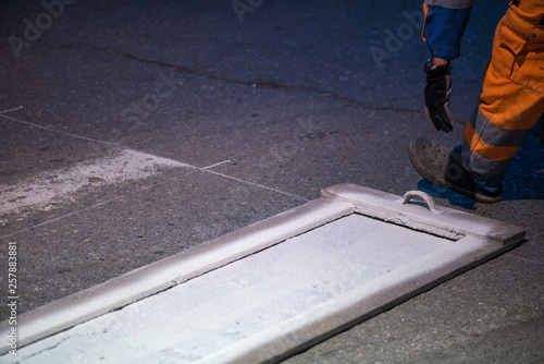Traffic line painting. Workers are painting white street lines on pedestrian crossing. Road cones with orange and white stripes in background, standing on asphalt during road construction works