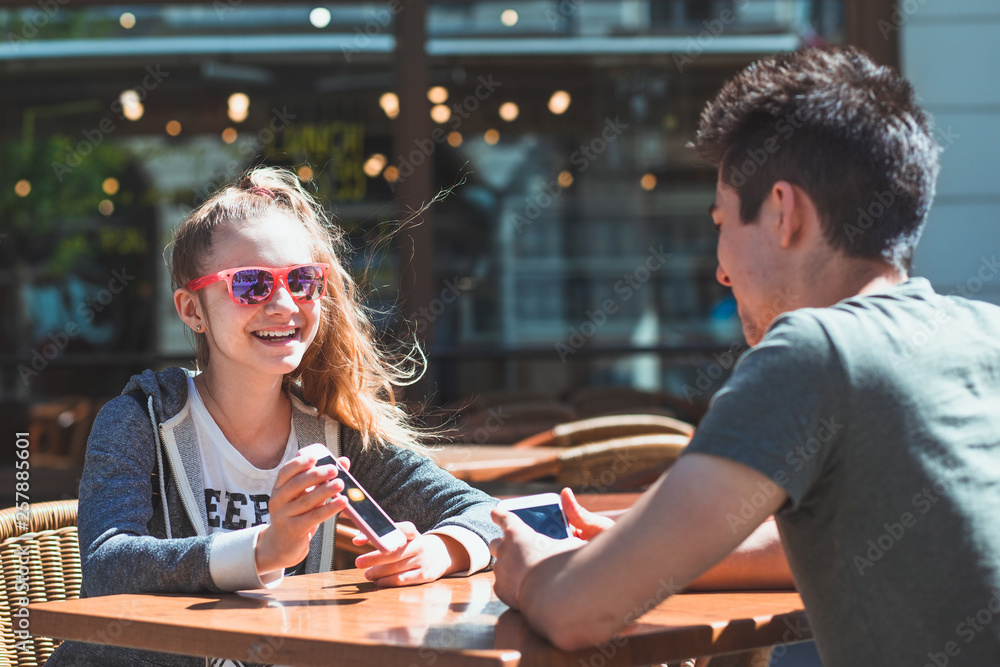 Fototapeta premium Young woman and man sitting in pavement cafe talking and using mobile phones