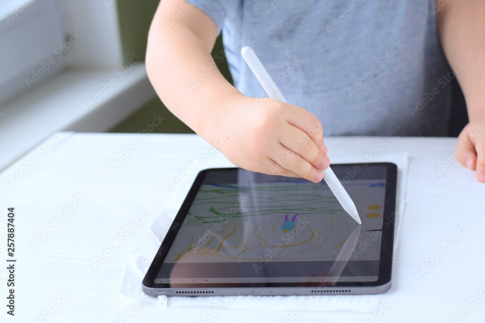 Portrait of a happiness cute little boy with new tablet. White caucasian smiling toddler boy drawing on tablet screen. Boy playing game on tablet on green blurred background and selective focus Portrait of a happiness cute little boy with new tablet. White caucasian smiling toddler boy drawing on tablet screen. Boy playing game on tablet on green blurred background and selective focus