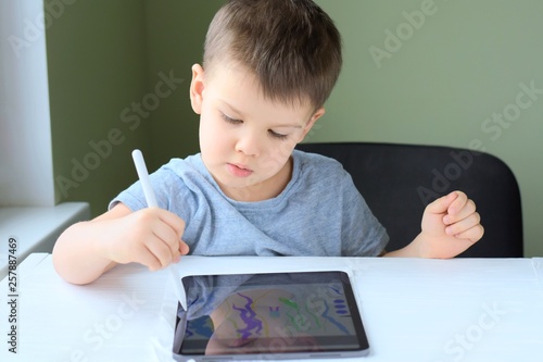 Portrait of a happiness cute little boy with new tablet. White caucasian smiling toddler boy drawing on tablet screen. Boy playing game on tablet on green blurred background and selective focus 