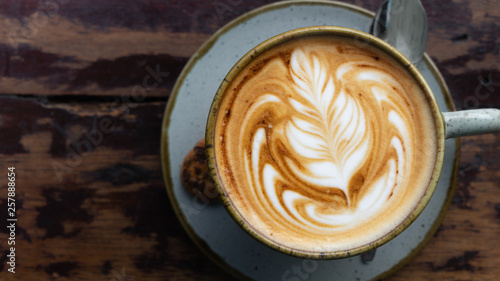 Top down shot of a perfectly made cappuccino made with locally grown coffee with a latte art rosetta on a worn wooden table framed to the right with a blurry background