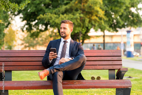 A businessmen sitting on a bench and using his smartphone