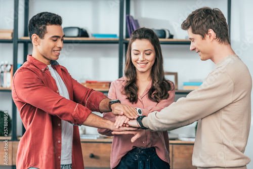 Three multicultural friends stacking hands together with smile at home