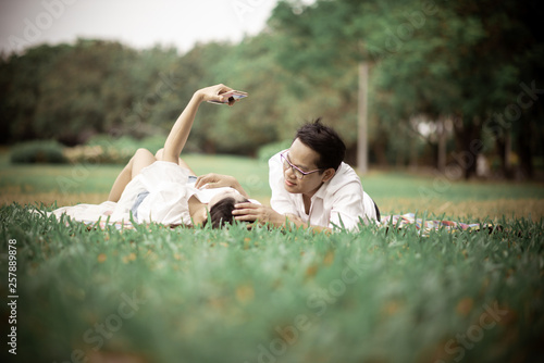 Portrait of happy young asian couple laying on grass In public park.