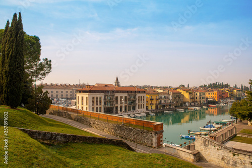 High angle view of the canal of Peschiera del Garda, an ancient town on the shore of Lake Garda, with the typical colored houses and moored boats in a sunny spring day, Veneto, Italy